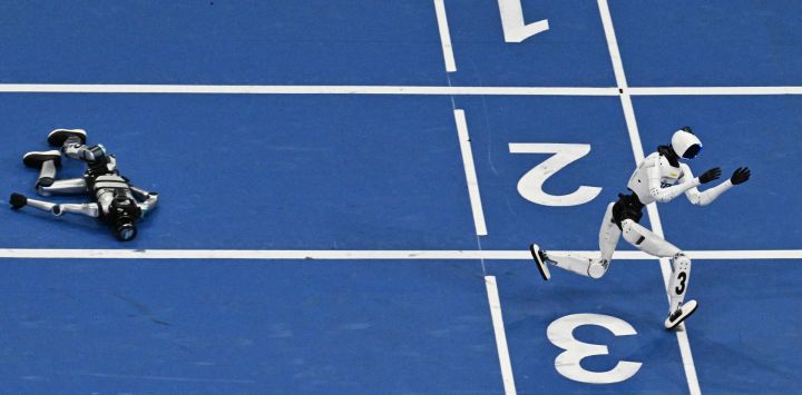 Un robot humanoide pasa corriendo junto a un competidor caído en la carrera de 400 metros durante el segundo día de los II Juegos Mundiales de Robots Humanoides en Pekín.