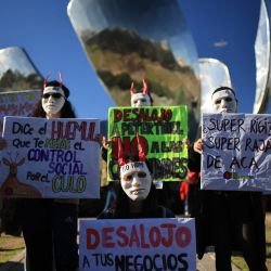 Manifestantes con máscaras y pancartas participan en una protesta contra Peter Thiel, presidente de Palantir Technologies, junto al monumento Floralis Generica en Buenos Aires. | Foto:Emiliano Lasalvia / AFP