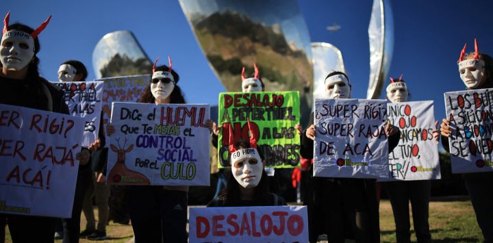 Manifestantes con máscaras y pancartas participan en una protesta contra Peter Thiel, presidente de Palantir Technologies, junto al monumento Floralis Generica en Buenos Aires.