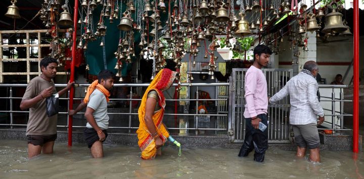 Varias personas caminan con dificultad por una calle inundada frente a un templo tras las fuertes lluvias en Varanasi, India.