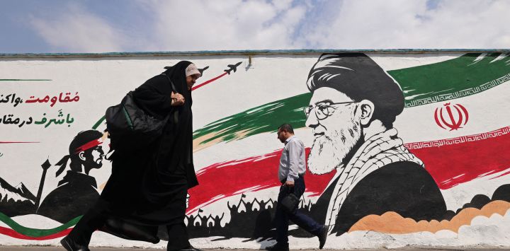 Los peatones pasan junto a un mural del asesinado líder supremo de Irán, el ayatolá Ali Jamenei, a lo largo de una calle en el centro de Teherán. Irán atacó objetivos militares estadounidenses en el Medio Oriente en represalia por los ataques estadounidenses en una isla en el Estrecho de Ormuz, el primer intercambio de disparos en un mes en una guerra que ha envuelto la región. Seis meses después del inicio del conflicto, las dos partes siguen en un punto muerto: Irán mantiene cerrado el estrecho estratégico y Washington persiste en un contrabloqueo naval contra Irán.