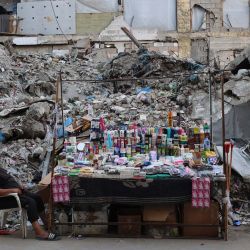 Un palestino se sienta junto a un puesto de cosméticos y productos para el hogar frente a un edificio destruido en la ciudad de Gaza. En octubre se alcanzó un alto el fuego en Gaza entre Israel y Hamás tras dos años de guerra, que se desencadenó por el ataque sin precedentes de milicianos palestinos contra Israel el 7 de octubre de 2023. La segunda fase del alto el fuego, que debía incluir el desarme de Hamás y la retirada gradual de las fuerzas israelíes de Gaza, lleva meses estancada. | Foto:OMAR AL-QATTAA / AFP