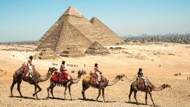 Imagen de turistas montando camellos en el complejo de las pirámides de Giza, en Egipto. Egipto es la cuna de una antigua civilización que floreció a lo largo del río Nilo. Desde las pirámides que han permanecido en pie durante milenios hasta sus bulliciosas ciudades modernas, lo antiguo y lo contemporáneo se entrelazan por todo el país, reflejando una civilización que ha perdurado a través de los siglos.