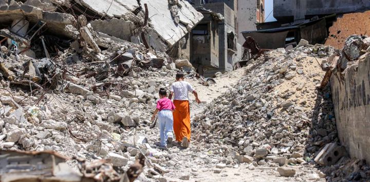 Dos niñas caminan entre los escombros de edificios derrumbados en Khan Yunis, al sur de la Franja de Gaza. El alto el fuego de octubre de 2025 redujo, pero no detuvo, la violencia en Gaza. Las operaciones israelíes han causado la muerte de 1288 personas desde que entró en vigor el alto el fuego, según el Ministerio de Salud de Gaza, que también opera bajo la autoridad de Hamás y cuyas cifras son consideradas fiables por las Naciones Unidas.