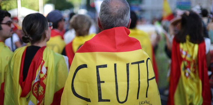 Un manifestante, envuelto en una bandera española con la inscripción "Ceuta siempre noble y leal", participa en una protesta un mes después de la llegada masiva de migrantes a Ceuta, frente al Parlamento español en Madrid. La indignación local divide a Ceuta un mes después de la llegada masiva de migrantes al territorio español del norte de África. Según el gobierno, unos 5.000 migrantes, o al menos 10.000 según las autoridades de Ceuta, permanecen en este pequeño territorio de 18,5 kilómetros cuadrados y 80.000 habitantes, vagando por las calles en busca de comida y durmiendo en la calle y en las playas.