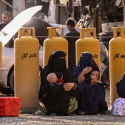 Mujeres afganas con burka, sosteniendo a sus hijos, se sientan en una gasolinera en el distrito de Fayzabad, provincia de Badakhshan. | Foto:OMER ABRAR / AFP
