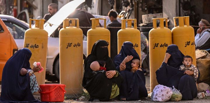 Mujeres afganas con burka, sosteniendo a sus hijos, se sientan en una gasolinera en el distrito de Fayzabad, provincia de Badakhshan.