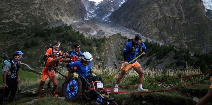 Un corredor de montaña compite en una joellette asistido por un grupo en la arista del Mont Favre durante la 23.ª edición del Ultra Trail du Mont Blanc (UTMB), una carrera de montaña de 174 km que atraviesa Francia, Italia y Suiza en Chamonix, al sureste de Francia.