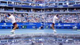 El argentino Francisco Cerundolo saca contra el belga Alexander Blockx, reflejado en el espejo de un equipo de televisión, durante su partido de octavos de final individuales masculinos en el noveno día del torneo de tenis US Open en el Centro Nacional de Tenis USTA Billie Jean King en la ciudad de Nueva York.