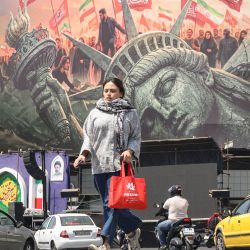 Una mujer cruza la calle mientras los automovilistas pasan junto a una valla publicitaria antiamericana en la plaza Enghelab de Teherán. Las fuerzas iraníes anunciaron que habían lanzado ataques contra objetivos militares estadounidenses en los Emiratos Árabes Unidos, Kuwait, Baréin y otros países de la región, prometiendo consecuencias "severas" ante la reanudación de los ataques estadounidenses contra la República Islámica. | Foto:ATTA KENARE / AFP