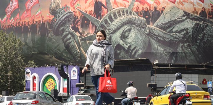 Una mujer cruza la calle mientras los automovilistas pasan junto a una valla publicitaria antiamericana en la plaza Enghelab de Teherán. Las fuerzas iraníes anunciaron que habían lanzado ataques contra objetivos militares estadounidenses en los Emiratos Árabes Unidos, Kuwait, Baréin y otros países de la región, prometiendo consecuencias "severas" ante la reanudación de los ataques estadounidenses contra la República Islámica.