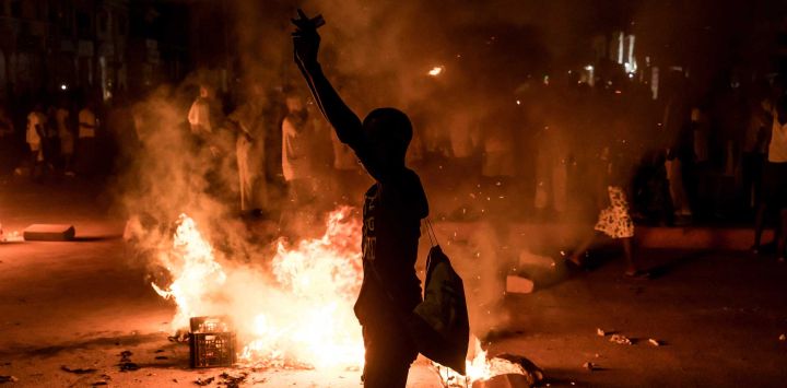 Un manifestante permanece junto a una barricada en llamas durante una protesta por la crisis eléctrica y los persistentes cortes de luz que afectan al país, en Brusubi. Miles de personas salieron a las calles durante la noche en Gambia, quemando neumáticos y coreando consignas contra el presidente en protesta por los apagones que aquejan al país desde junio y que recientemente se han agravado. Los cortes de electricidad rotativos, que se producen durante la temporada de calor, han llegado a durar hasta 48 horas en algunas zonas.