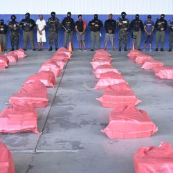 Agentes de policía custodian a cuatro personas detenidas tras una incautación de cocaína, mientras se exhiben los paquetes de la droga en la Base Aérea Hernán Acosta Mejía de Tegucigalpa, Honduras. La Marina y la Fuerza Aérea de Honduras interceptaron una embarcación en aguas del Caribe que transportaba 1,6 toneladas de cocaína y capturaron a sus cuatro tripulantes hondureños, según informó el Ministerio Público. | Foto:Orlando Sierra / AFP