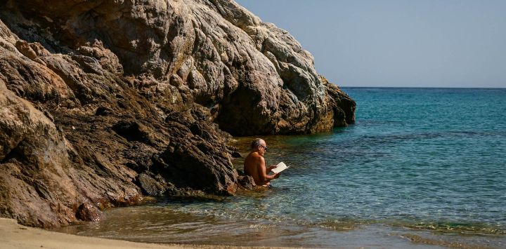 Un hombre lee un libro mientras disfruta de una mañana soleada en una playa de la isla griega del Egeo de Ikaria.