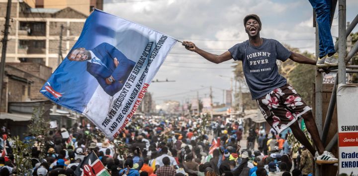 Un partidario de Edwin Sifuna —figura de la oposición keniana y senador por Nairobi—, perteneciente a la coalición Linda Mwananchi (Proteger a los Ciudadanos), sostiene una bandera que presenta a Sifuna como el próximo presidente de Kenia, mientras una gran multitud sigue una caravana opositora en Nairobi.