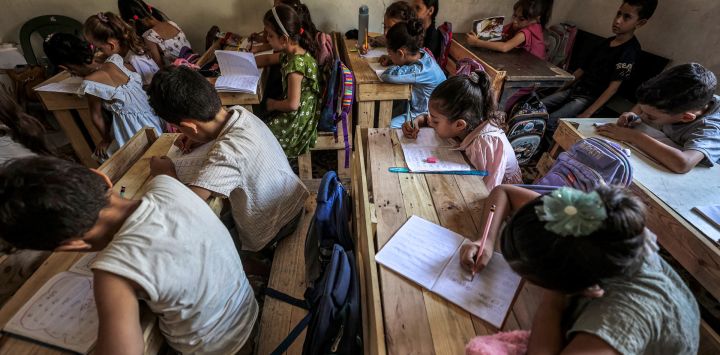 Alumnos palestinos asisten a clase en una escuela de la ciudad de Gaza, sentados en pupitres fabricados con palés de madera reutilizados y restos de madera. Desde que estalló la guerra en Gaza en octubre de 2023, la gran mayoría de las escuelas y centros educativos de la Franja han sufrido daños o han sido destruidos por ataques aéreos o de artillería, dejando a decenas de miles de niños sin acceso a una educación formal.