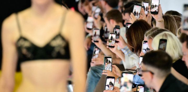 Los asistentes sostienen sus teléfonos inteligentes durante el desfile de la colección de Prada, en el marco de la Semana de la Moda de Milán (temporada Primavera/Verano 2027 para mujer).