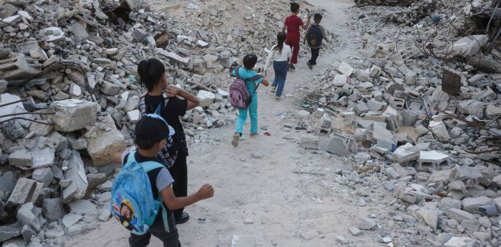 Niños palestinos caminan hacia la escuela entre los escombros de edificios destruidos al comenzar el año escolar en Jan Yunis, en el sur de la Franja de Gaza.