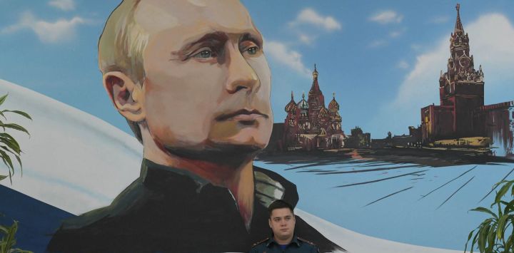 Un miembro del Ministerio de Emergencias de Rusia está sentado bajo un mural que representa al presidente ruso, Vladímir Putin, durante las elecciones parlamentarias de Rusia en un colegio electoral de Donetsk, zona de Ucrania bajo control ruso, en medio del conflicto ruso-ucraniano en curso.