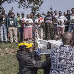 Miembros de la comunidad ayudan a cargar el cuerpo de una víctima en una furgoneta funeraria mientras otros observan, tras un tiroteo masivo en la zona de Ziko, en KwaMakhutha, al sur de Durban. Hombres armados irrumpieron en una vivienda de la ciudad sudafricana de Durban y mataron a 11 personas, según informó el jefe del gobierno local. | Foto:RAJESH JANTILAL / AFP
