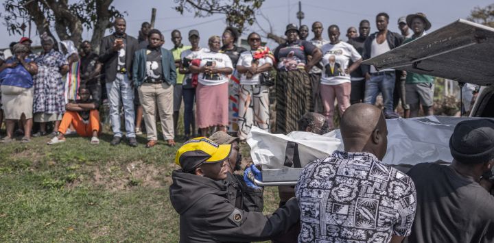 Miembros de la comunidad ayudan a cargar el cuerpo de una víctima en una furgoneta funeraria mientras otros observan, tras un tiroteo masivo en la zona de Ziko, en KwaMakhutha, al sur de Durban. Hombres armados irrumpieron en una vivienda de la ciudad sudafricana de Durban y mataron a 11 personas, según informó el jefe del gobierno local.