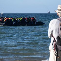 Un turista observa a migrantes a bordo de una embarcación de traficantes que intentan cruzar el canal de la Mancha bajo la vigilancia de los servicios de rescate franceses, frente a la playa de Merville-Franceville-Plage, en el noroeste de Francia. A medida que las travesías por el canal de la Mancha se vuelven cada vez más difíciles desde las playas del norte de Francia, los migrantes prueban nuevas rutas para llegar a Inglaterra desde regiones del sur, como el departamento de Calvados, donde el canal es más ancho que a lo largo de la costa septentrional francesa. | Foto:Guillaume Saligot / AFP