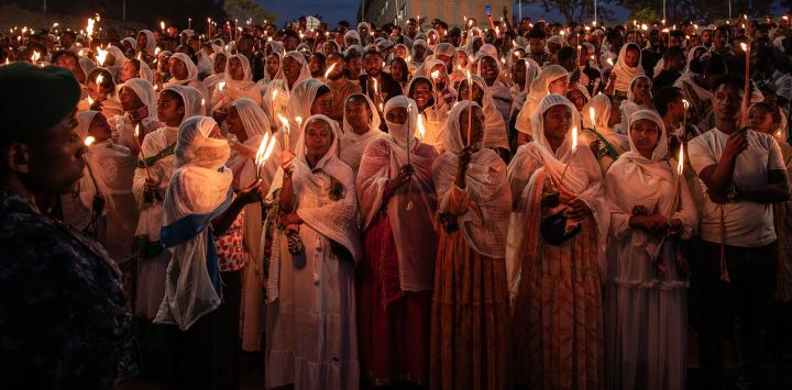 Los creyentes ortodoxos etíopes vestidos con ropa blanca tradicional sostienen velas encendidas al atardecer durante las celebraciones de Meskel en la Plaza Meskel en Addis Abeba. La celebración etíope de Meskel es una fiesta religiosa anual en la iglesia ortodoxa etíope que conmemora el descubrimiento de la Verdadera Cruz en el siglo IV por la emperatriz romana Helena.