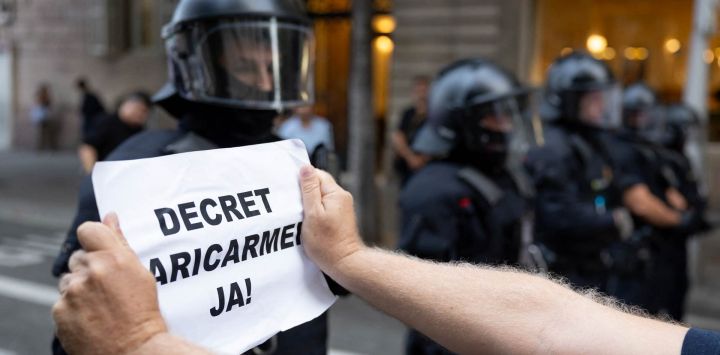 Un manifestante sostiene un cartel con el lema "¡Decreto Maricarmen ya!" frente a las fuerzas policiales durante una protesta con motivo de la visita del presidente del Gobierno español, en plena crisis de la vivienda en España, en Barcelona (Cataluña). Se espera que el gobierno del presidente socialista apruebe un paquete de medidas denominado "decreto Maricarmen", tras el desahucio la semana pasada de Maricarmen Abascal, una mujer de 87 años, de la que había sido su vivienda de toda la vida. Según se ha informado, la medida incluirá la renovación automática de los contratos de alquiler y mayores restricciones a los desahucios.