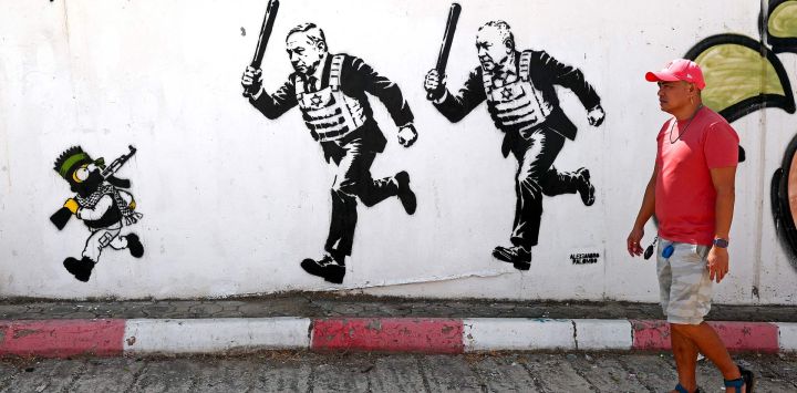 Un hombre pasa frente a un mural titulado "RUN" (Corre), obra del artista Alexsandro Palombo, que representa al primer ministro israelí Benjamin Netanyahu (centro) y al político Gadi Eisenkot —ataviados con chalecos antibalas y portando porras— persiguiendo a Bart Simpson, caracterizado como un joven combatiente de Hamás, en Tel Aviv.