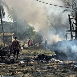Personas caminan entre el humo y los escombros humeantes tras un ataque aéreo militar contra un mercado y un puente adyacente en Kyauktaw, en el oeste del estado de Rakáin. Un ataque aéreo militar contra un mercado en el oeste de Myanmar causó la muerte de 33 personas e hirió a otras 36, según informó en un comunicado una facción rebelde que controla la zona. | Foto:AFP