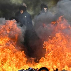 Estudiantes que protestan permanecen frente a una barricada quemada durante una acción de bloqueo a las puertas del instituto Le Corbusier, en Aubervilliers (al norte de París). Desde finales de septiembre, los estudiantes han protagonizado protestas frente a los centros educativos por diversas quejas, que van desde los horarios, el tamaño de las clases y la falta de profesores hasta el calor excesivo en las aulas durante las olas de calor de este año. | Foto:LOU BENOIST / AFP