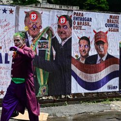 Un hombre disfrazado del Joker pasa frente a un muro con imágenes del presidente de Estados Unidos, Donald Trump, y del senador derechista y candidato presidencial del Partido Liberal (PL) de Brasil, Flavio Bolsonaro, durante las elecciones presidenciales en la Avenida Paulista de São Paulo, Brasil. | Foto:PABLO PORCIUNCULA / AFP