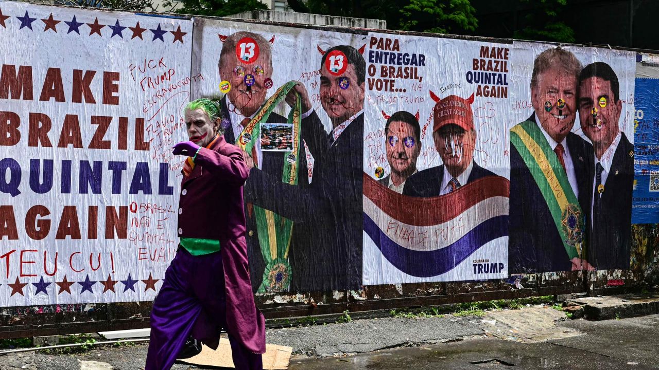 Un hombre disfrazado del Joker pasa frente a un muro con imágenes del presidente de Estados Unidos, Donald Trump, y del senador derechista y candidato presidencial del Partido Liberal (PL) de Brasil, Flavio Bolsonaro, durante las elecciones presidenciales en la Avenida Paulista de São Paulo, Brasil. | Foto:PABLO PORCIUNCULA / AFP