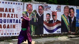 Un hombre disfrazado del Joker pasa frente a un muro con imágenes del presidente de Estados Unidos, Donald Trump, y del senador derechista y candidato presidencial del Partido Liberal (PL) de Brasil, Flavio Bolsonaro, durante las elecciones presidenciales en la Avenida Paulista de São Paulo, Brasil.