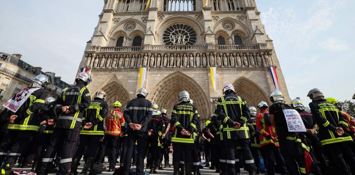 Bomberos guardan un minuto de silencio en memoria de sus compañeros fallecidos mientras combatían incendios forestales en Francia, frente a la catedral de Notre-Dame de París, durante una protesta convocada por una amplia coalición de sindicatos que reclaman mejores salarios y mayores recursos presupuestarios, en París.