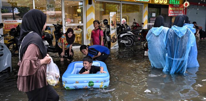 Las familias juegan en las aguas inundadas a lo largo de la carretera Ramkhamhaeng en el distrito de Bang Kapi, Bangkok. Las profundas inundaciones en Bangkok llevaron a miles de residentes a refugios mientras otros se apresuraban a comprar comestibles o secar sus hogares después de días de fuertes lluvias que inundaron mercados, carreteras y residencias.