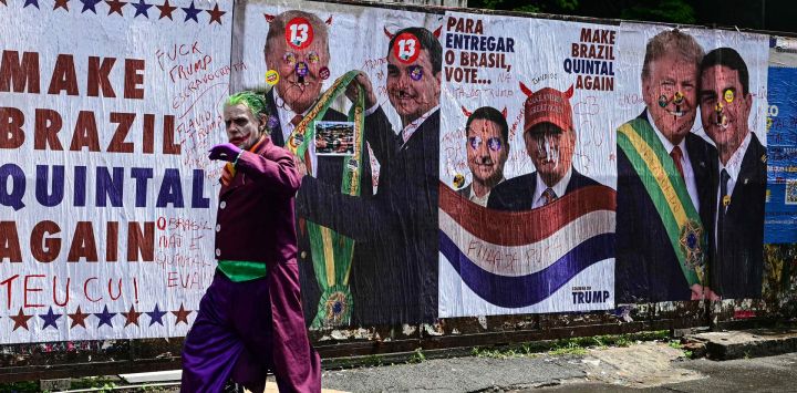 Un hombre disfrazado del Joker pasa frente a un muro con imágenes del presidente de Estados Unidos, Donald Trump, y del senador derechista y candidato presidencial del Partido Liberal (PL) de Brasil, Flavio Bolsonaro, durante las elecciones presidenciales en la Avenida Paulista de São Paulo, Brasil.