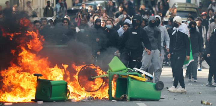 Un estudiante arroja basura a una hoguera mientras otros estudiantes manifestantes llevan a cabo un bloqueo cerca de la Place de la Nation, en París. Desde finales de septiembre, los estudiantes han protagonizado protestas frente a los centros educativos debido a diversas quejas, que van desde los horarios, el tamaño de las clases y la falta de profesores hasta el calor excesivo en las aulas durante las olas de calor de este año. Las protestas comenzaron en la región de Île-de-France, en los alrededores de París, pero se han extendido a otras ciudades de todo el país.