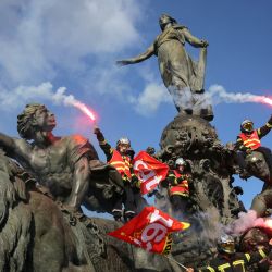 Bomberos ondean bengalas y banderas del sindicato francés Confederación General del Trabajo (CGT) mientras trepan por la estatua "El Triunfo de la República" en la plaza de la Nación, en París, durante una concentración para exigir recursos adicionales tras un verano de incendios forestales récord. | Foto:Thomas Samson / AFP