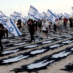 Personas que portan banderas de Israel caminan a través de una instalación conmemorativa montada en la playa de Tel Aviv para recordar el tercer aniversario del ataque de Hamás contra Israel. Israel conmemoró el tercer aniversario del ataque de Hamás del 7 de octubre con homenajes en silencio, nuevos ataques contra Gaza e intensos debates políticos, semanas antes de unas elecciones en las que el día más mortífero en la historia del país ocupará un lugar central. | Foto:JACK GUEZ / AFP