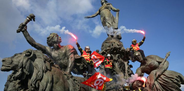 Bomberos ondean bengalas y banderas del sindicato francés Confederación General del Trabajo (CGT) mientras trepan por la estatua "El Triunfo de la República" en la plaza de la Nación, en París, durante una concentración para exigir recursos adicionales tras un verano de incendios forestales récord.
