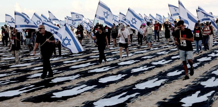 Personas que portan banderas de Israel caminan a través de una instalación conmemorativa montada en la playa de Tel Aviv para recordar el tercer aniversario del ataque de Hamás contra Israel. Israel conmemoró el tercer aniversario del ataque de Hamás del 7 de octubre con homenajes en silencio, nuevos ataques contra Gaza e intensos debates políticos, semanas antes de unas elecciones en las que el día más mortífero en la historia del país ocupará un lugar central.