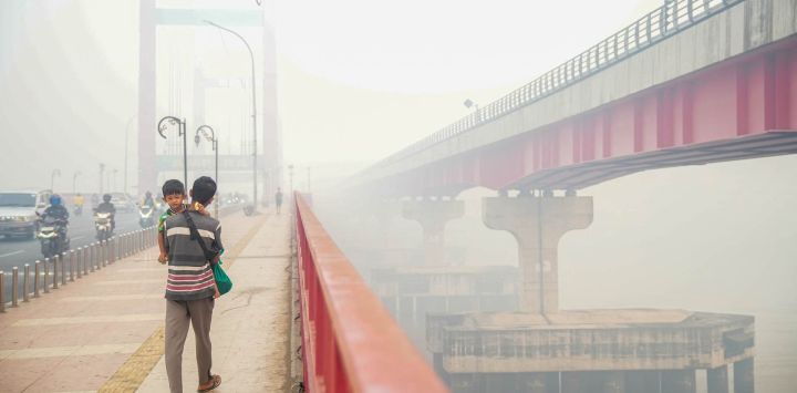 Un hombre que lleva a un niño en brazos camina por el puente Ampera en Palembang, Sumatra Meridional, mientras la bruma provocada por los incendios forestales y de terrenos en la región cubre el cielo y las zonas circundantes. Durante semanas, Indonesia ha estado combatiendo incendios que han arrasado vastas extensiones de bosques y ecosistemas de turberas, provocando que una bruma tóxica cubra partes del país, así como Malasia y Singapur. 
