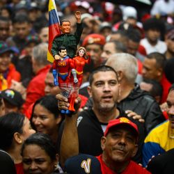 Un partidario del gobierno de Venezuela sostiene figuras que representan al fallecido presidente Hugo Chávez, al presidente Nicolás Maduro —caracterizado como "Super Bigote"— y a la primera dama Cilia Flores, durante una marcha para conmemorar el aniversario de la última victoria electoral de Chávez en 2012, en Caracas. | Foto:Maxwell Briceno / AFP