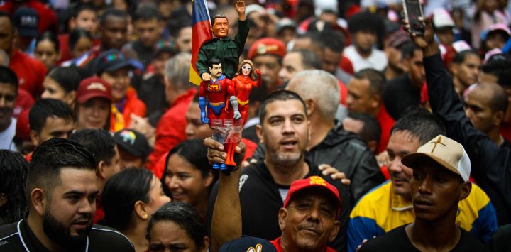 Un partidario del gobierno de Venezuela sostiene figuras que representan al fallecido presidente Hugo Chávez, al presidente Nicolás Maduro —caracterizado como "Super Bigote"— y a la primera dama Cilia Flores, durante una marcha para conmemorar el aniversario de la última victoria electoral de Chávez en 2012, en Caracas.