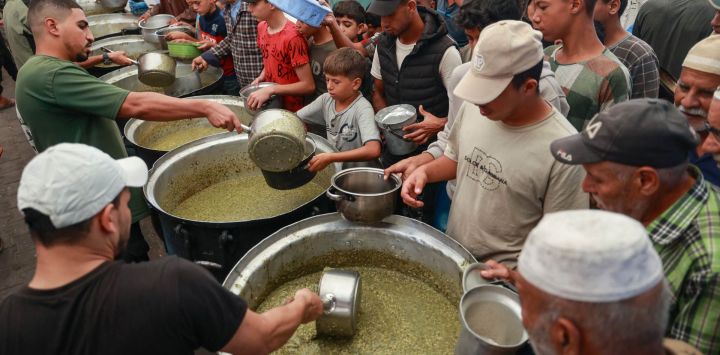 Palestinos desplazados reciben comidas calientes distribuidas por una cocina benéfica en el campamento de refugiados de Nuseirat, en el centro de la Franja de Gaza.