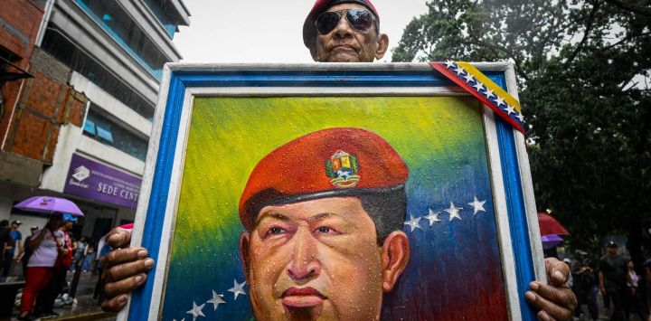 Un partidario del gobierno de Venezuela porta un retrato del fallecido presidente Hugo Chávez durante una marcha para conmemorar el aniversario de su última victoria electoral en 2012, en Caracas.