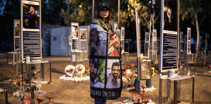 Una persona en duelo sostiene un cartel con retratos de las víctimas mientras permanece en el lugar del festival de música Nova, en Re'im (sur de Israel), para conmemorar el tercer aniversario del ataque de Hamás.