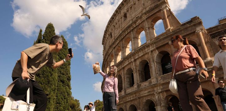 Imagen de una turista china posando con un libro de texto de una escuela secundaria china con el Coliseo en la portada, frente al Coliseo, en Roma, Italia.