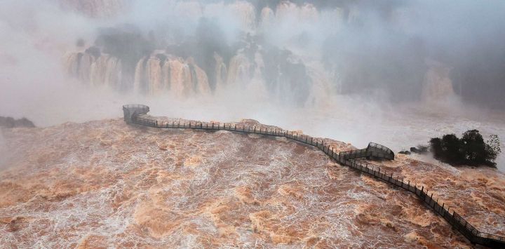 Una vista general muestra la pasarela para visitantes en las cataratas del Iguazú, situada sobre una fuerte corriente y vista desde el lado brasileño de la triple frontera entre Brasil, Argentina y Paraguay —en la ciudad de Foz do Iguaçu, estado de Paraná, Brasil. Las autoridades cerraron temporalmente el acceso turístico a las cataratas del Iguazú debido a la crecida del río homónimo, al tiempo que se registraron aumentos en el caudal de los ríos Paraná y Uruguay como consecuencia de las lluvias asociadas al fenómeno de El Niño.